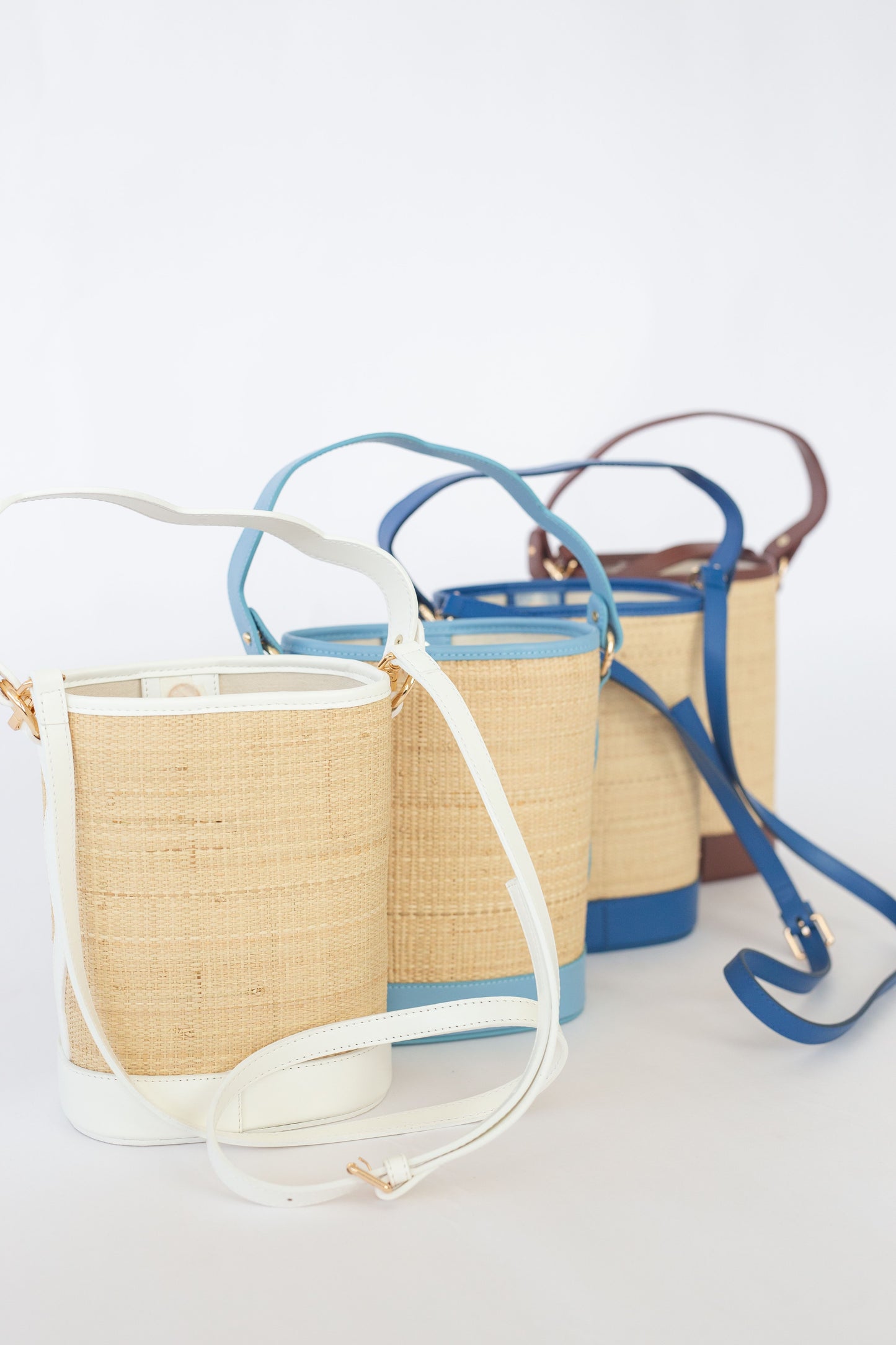 Three woven handbags with a variety of color straps on a white background