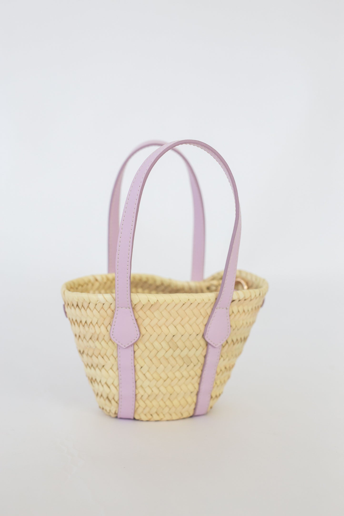 Woven basket with lilac handles on a light gray background