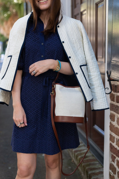 Woman in a navy dress with a white jacket and brown handbag standing outdoors.