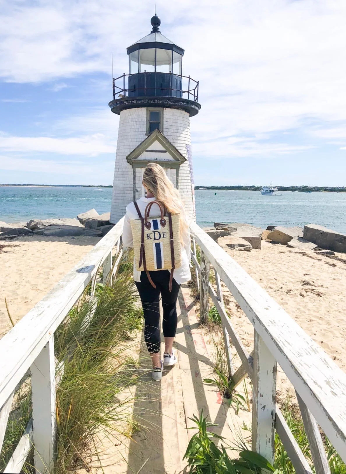 Chic vacation styling featuring the Phebe custom monogrammed rattan backpack at a lighthouse on Nantucket.