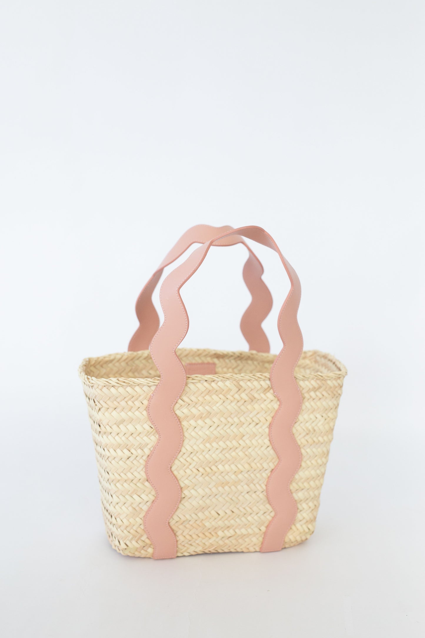 Woven basket with pink decorative handles on a white background