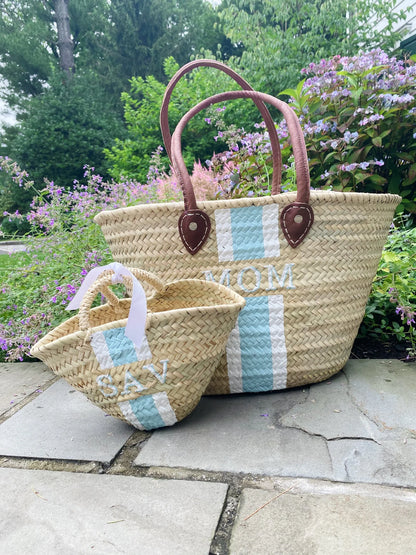 Woven tote bag with 'MOM' and matching baby tote, outdoors on stone path.