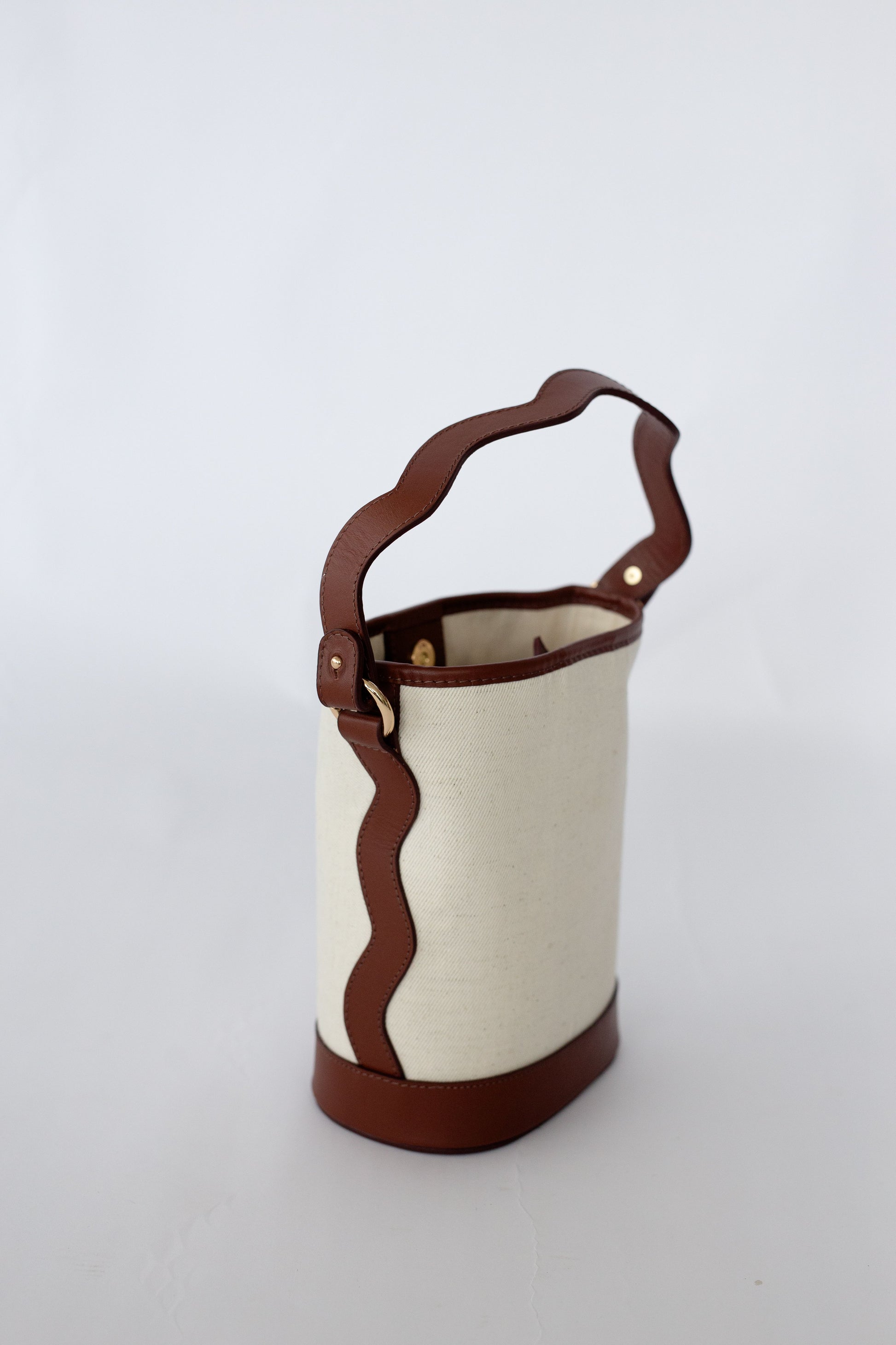 White canvas bucket bag with brown leather handle on a white background
