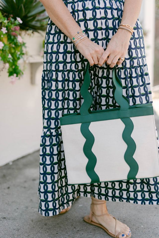 Close-up of a model in a navy geometric print maxi dress holding the Breck and Grier Grier Tote bag, featuring cream canvas and forest green scalloped leather trim.