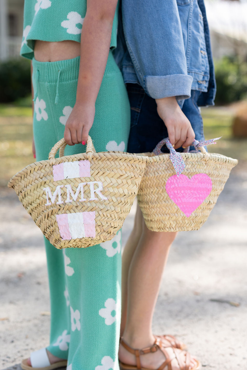 Two people holding handwoven palm leaf mini basket bags featuring a custom painted heart design and a custom monogram