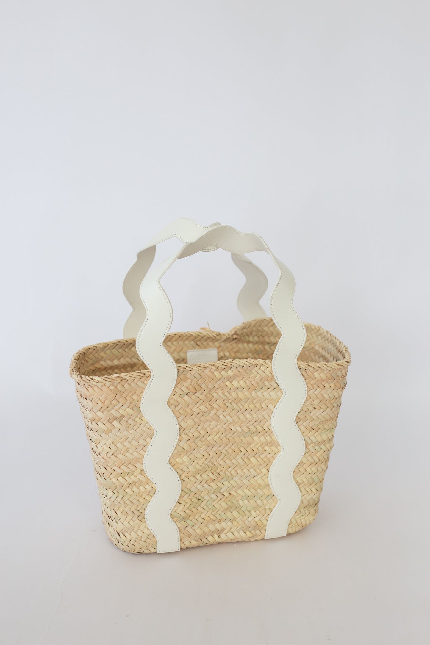 Woven basket with white handle on a light gray background