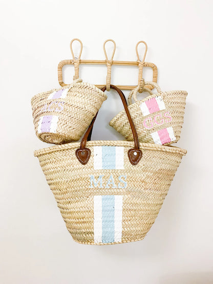 The Mommy and Me matching personalized straw travel bags resting together on a rack, evoking a luxury family vacation vibe.