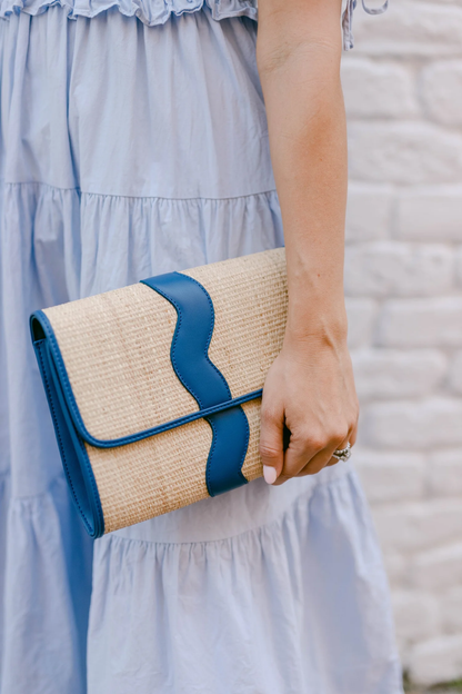 Person holding a straw clutch with blue leather accents against a light background