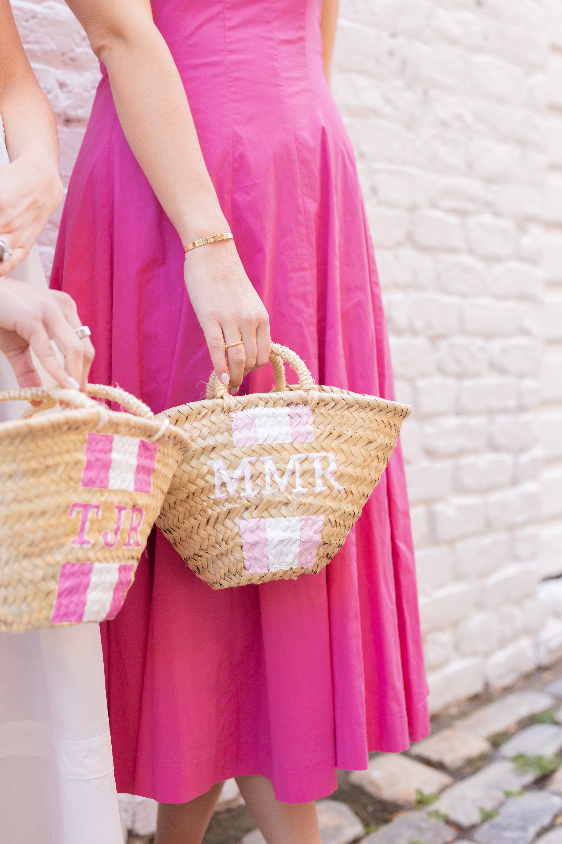 The personalized Quinn mini straw travel purses in the hands of two women in pink vacation outfits, evoking a luxury summer vacation aesthetic.
