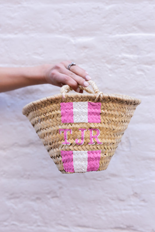 A beautiful flat-lay photo of the custom hand-painted Quinn mini straw travel bag with pink and white colorway.