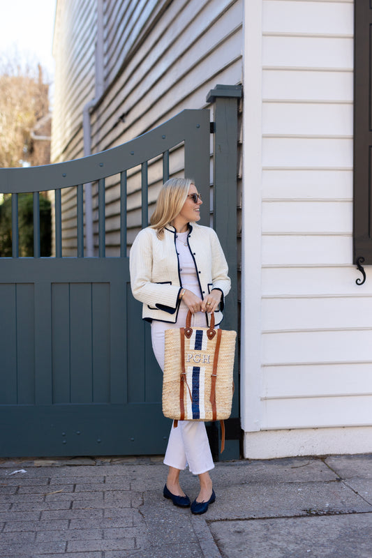 Model wearing a white jacket and white jeans showing the hands-free back straps of the Phebe personalized rattan backpack.