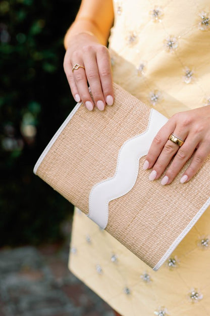 Close-up of a person holding a rattan White clutch, wearing a gold dress.