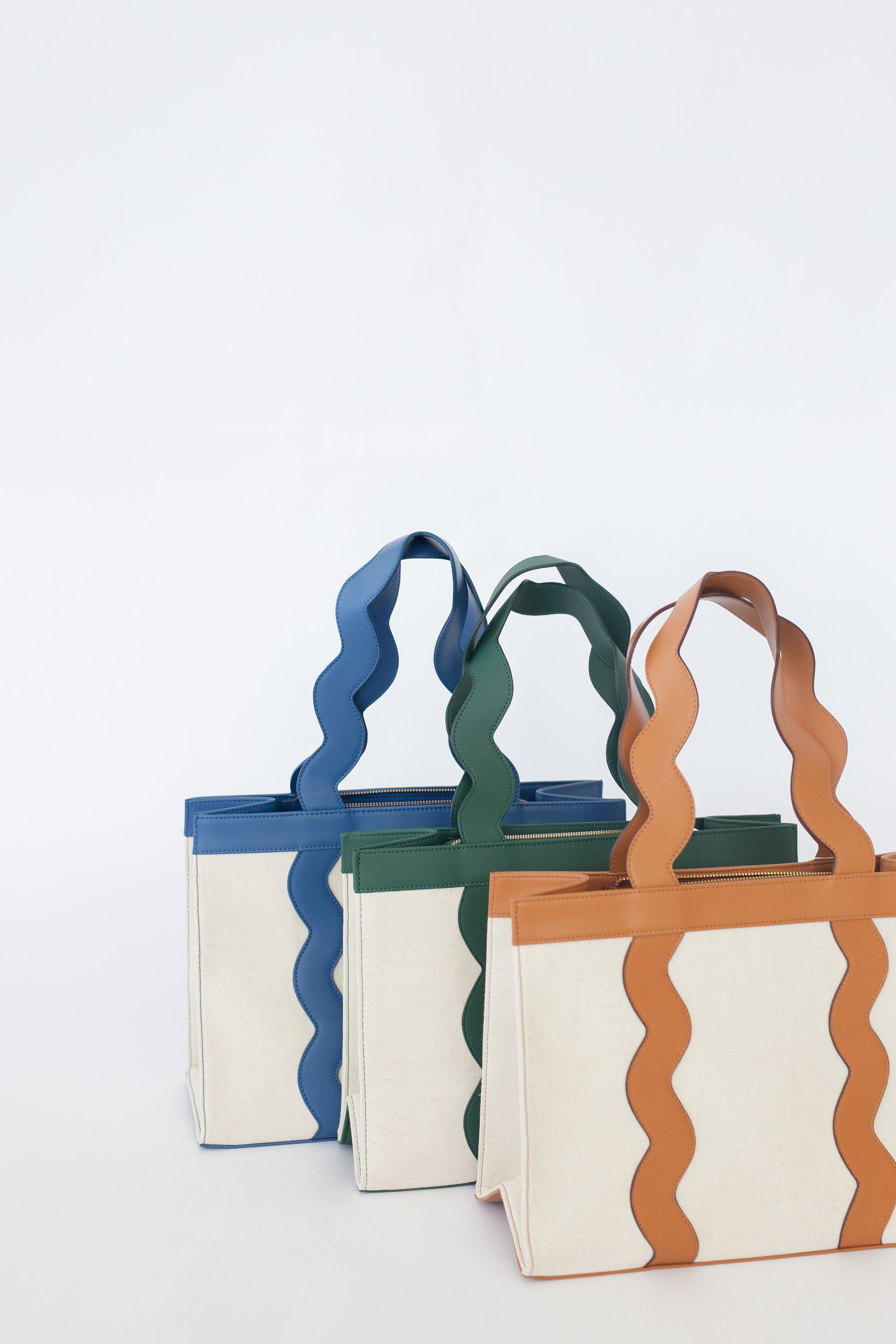 Three colorful tote bags with wavy handles on a white background