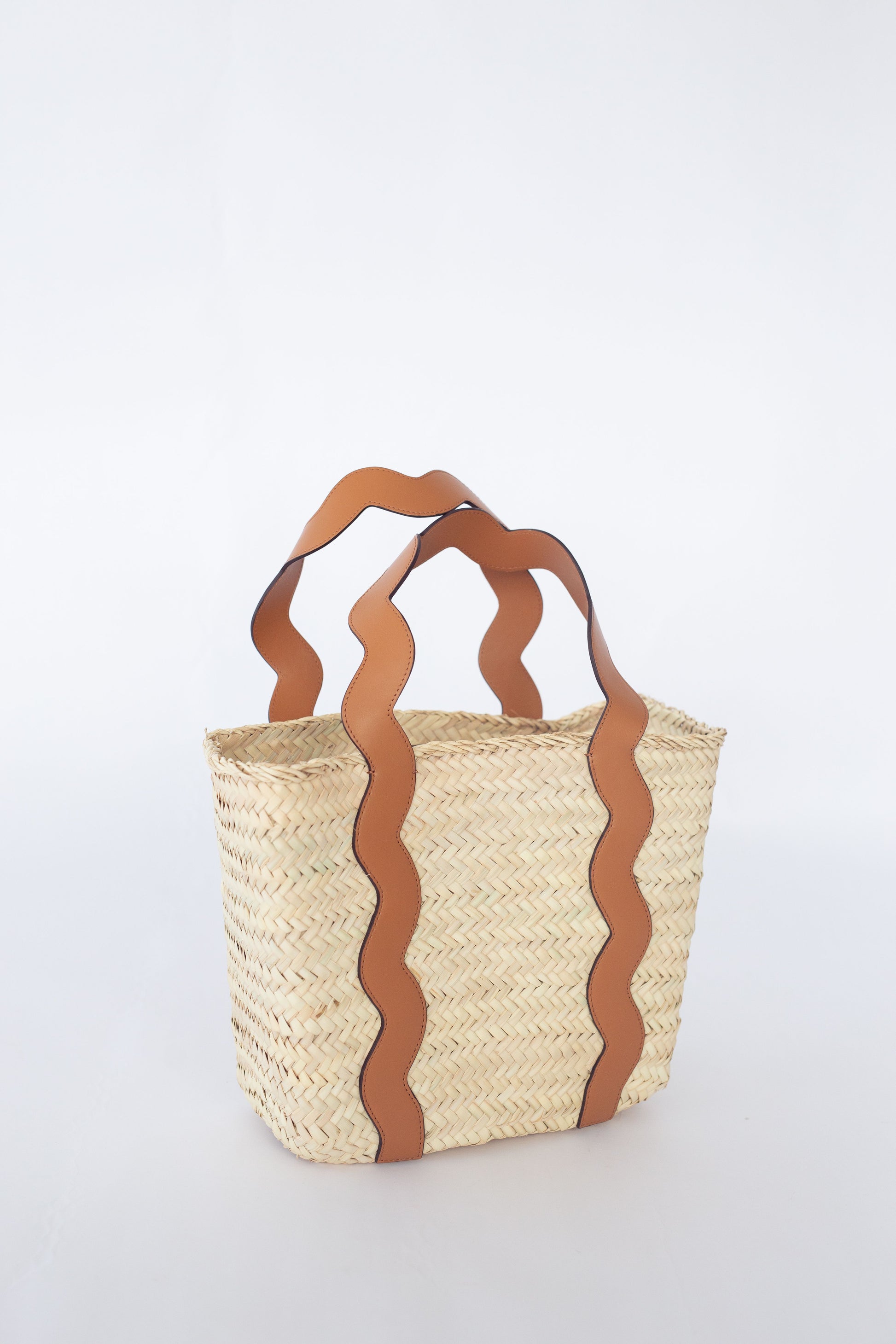 Woven basket with brown leather handles on a white background