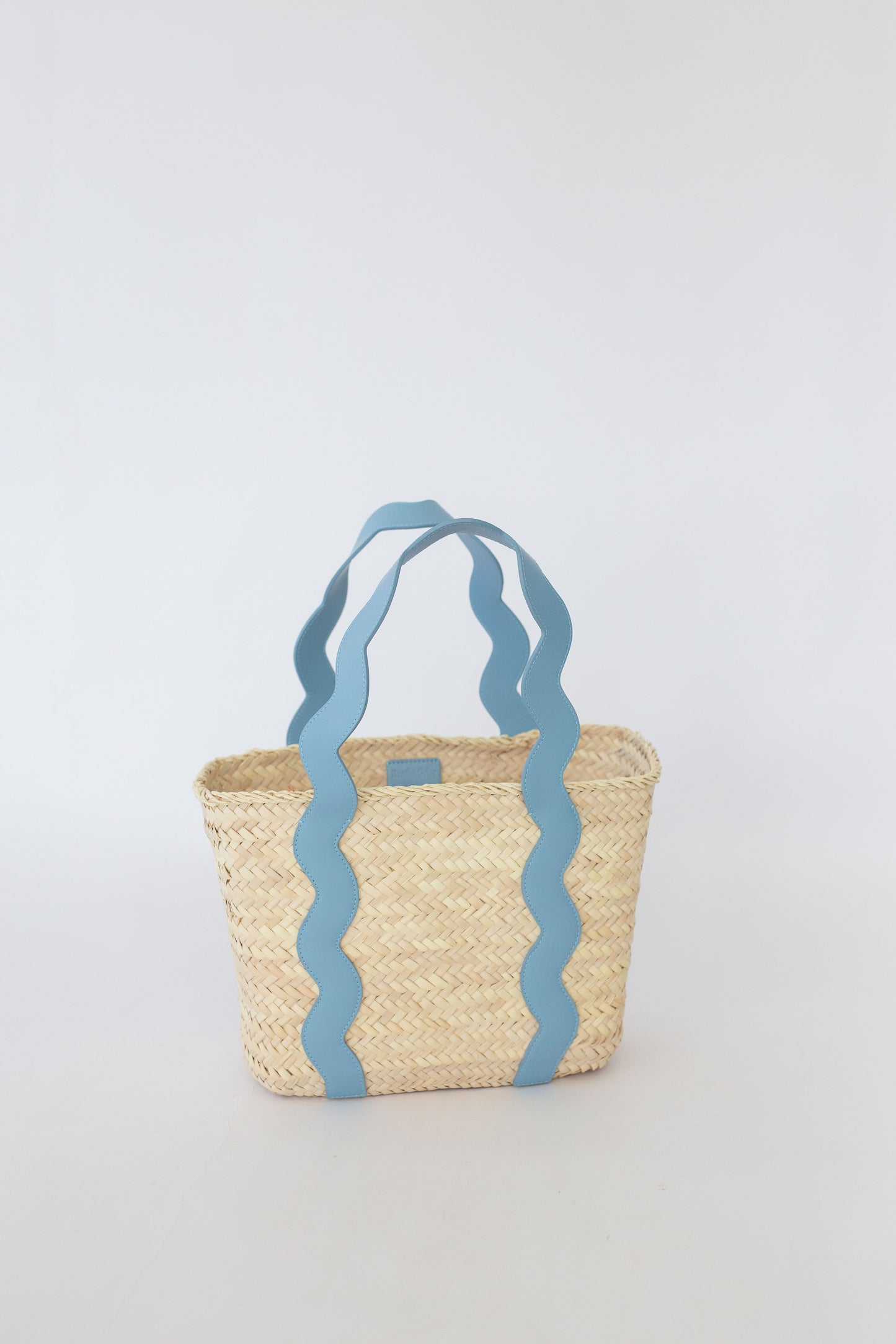 Woven basket with blue wavy handles on a light gray background