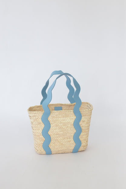 Woven basket with blue wavy handles on a light gray background