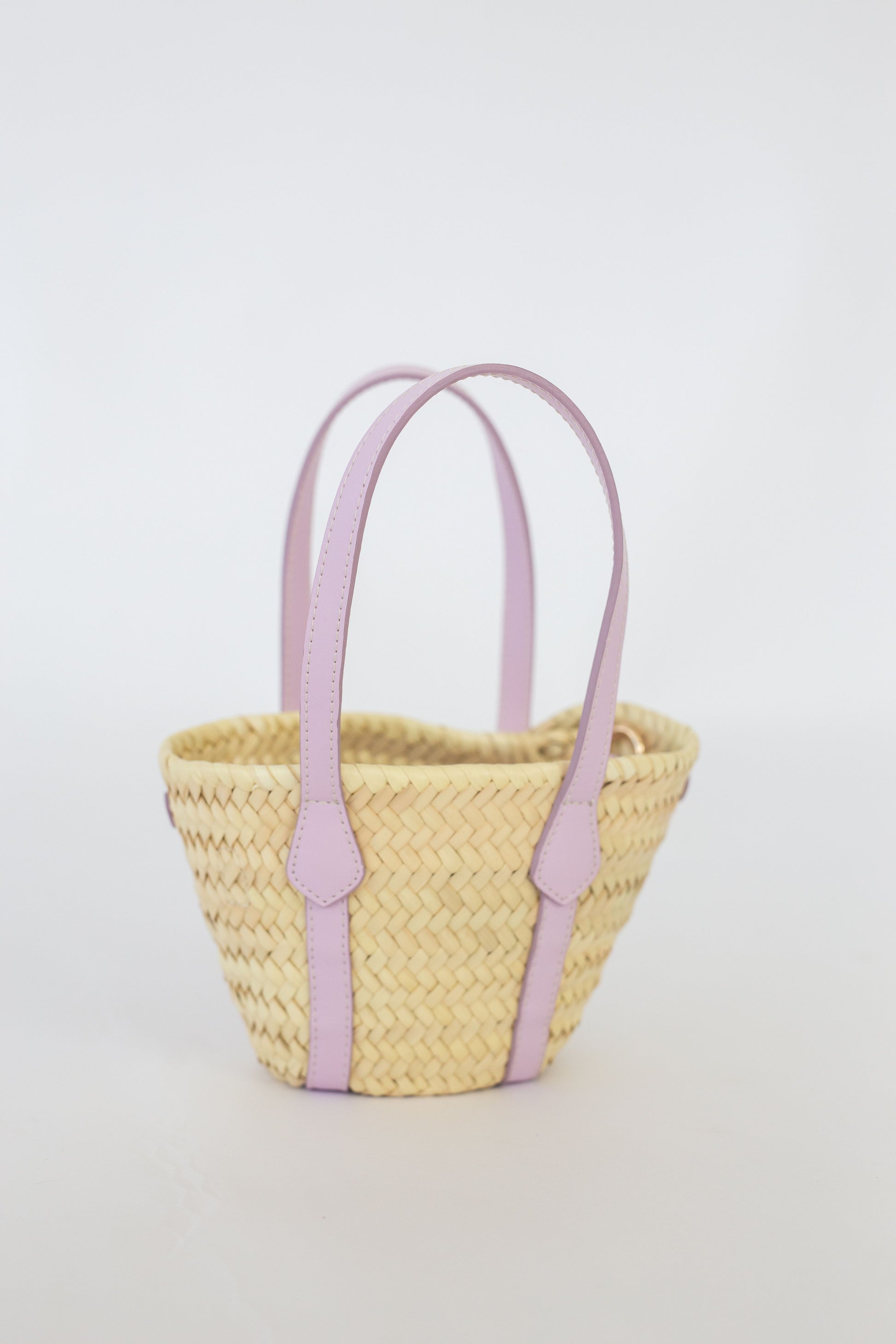 Woven basket with lilac handles on a light gray background
